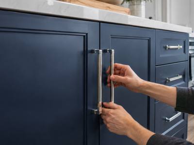 A hand fitting a chrome handle to a navy painted cabinet door.