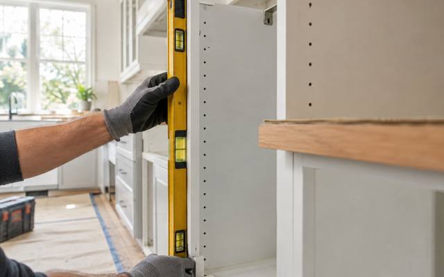 An installer holding a level against a cabinet box.